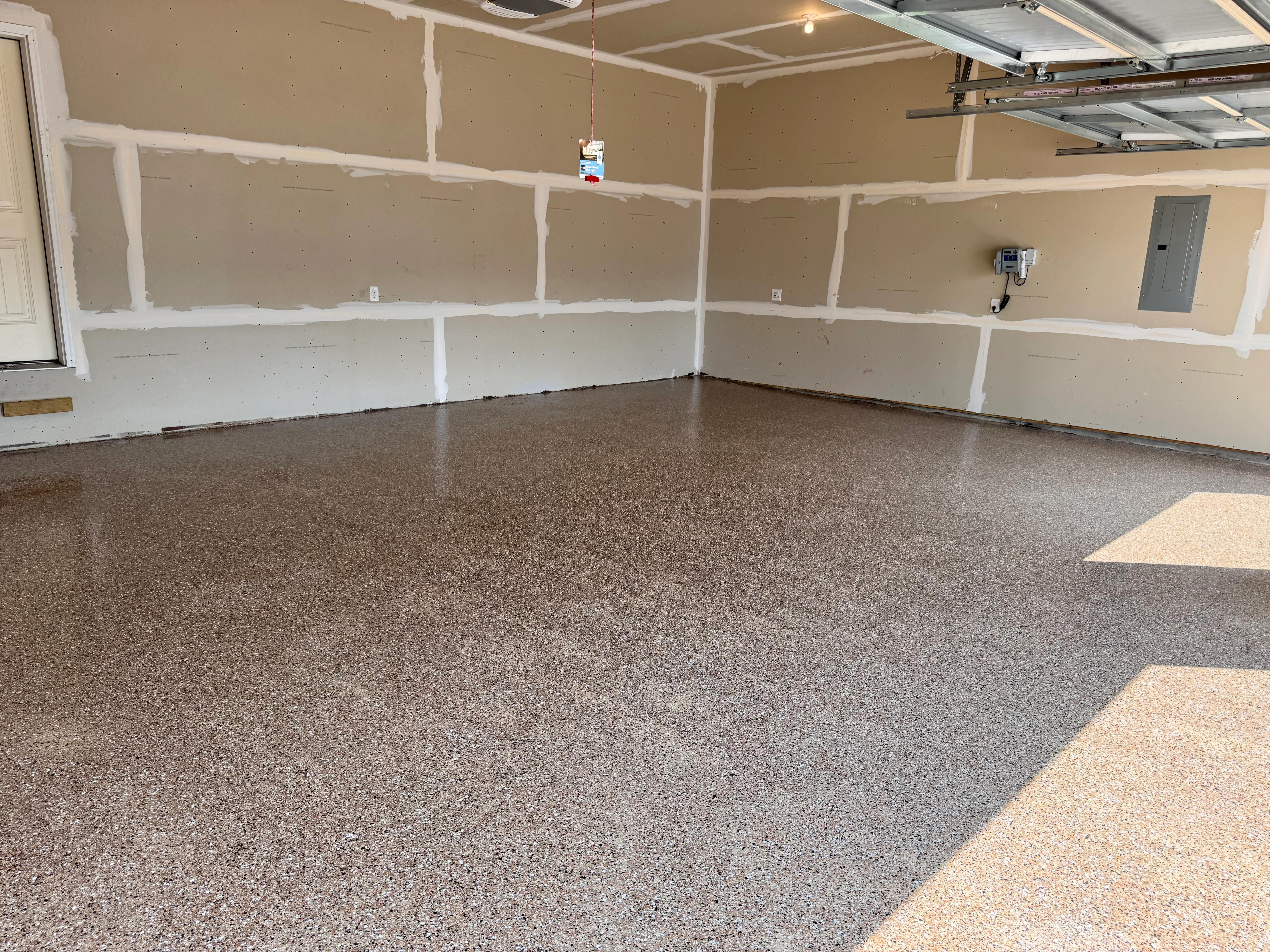 Gray speckled epoxy garage floor with white drywall framing and metal garage door tracks