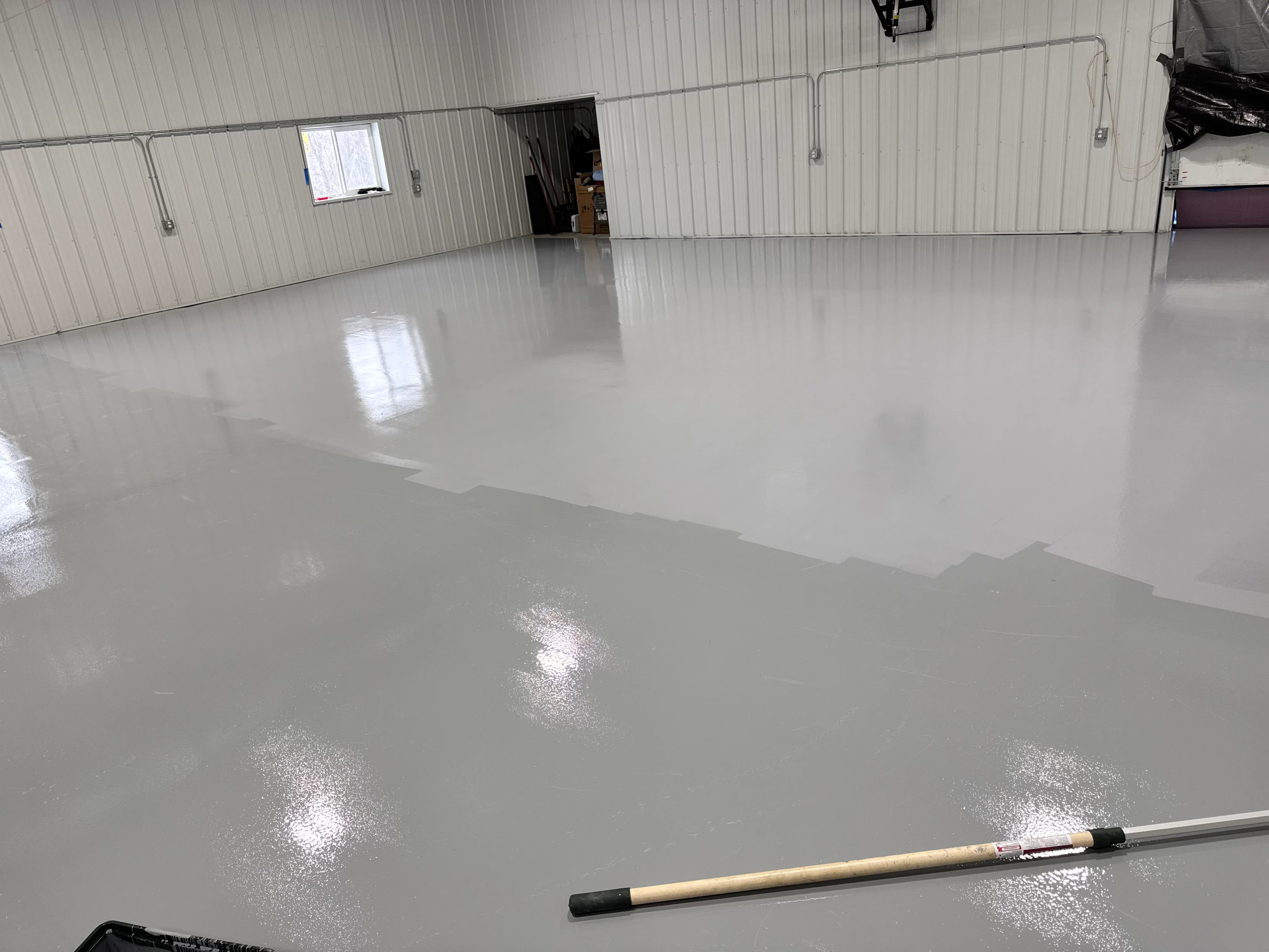 Newly installed gray epoxy floor in commercial garage with reflective finish and metal walls