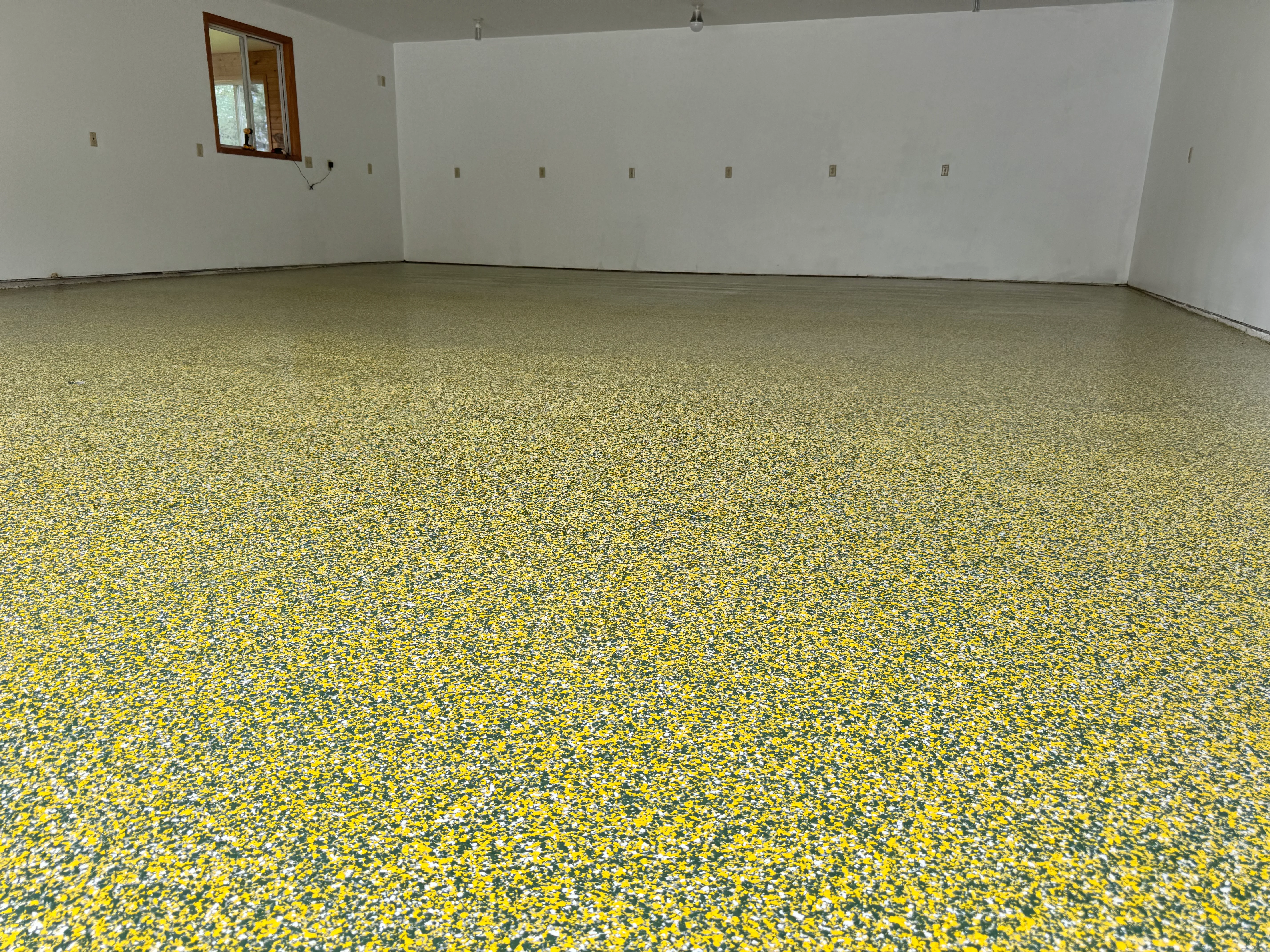Yellow and gray speckled epoxy floor in finished garage with white drywall walls