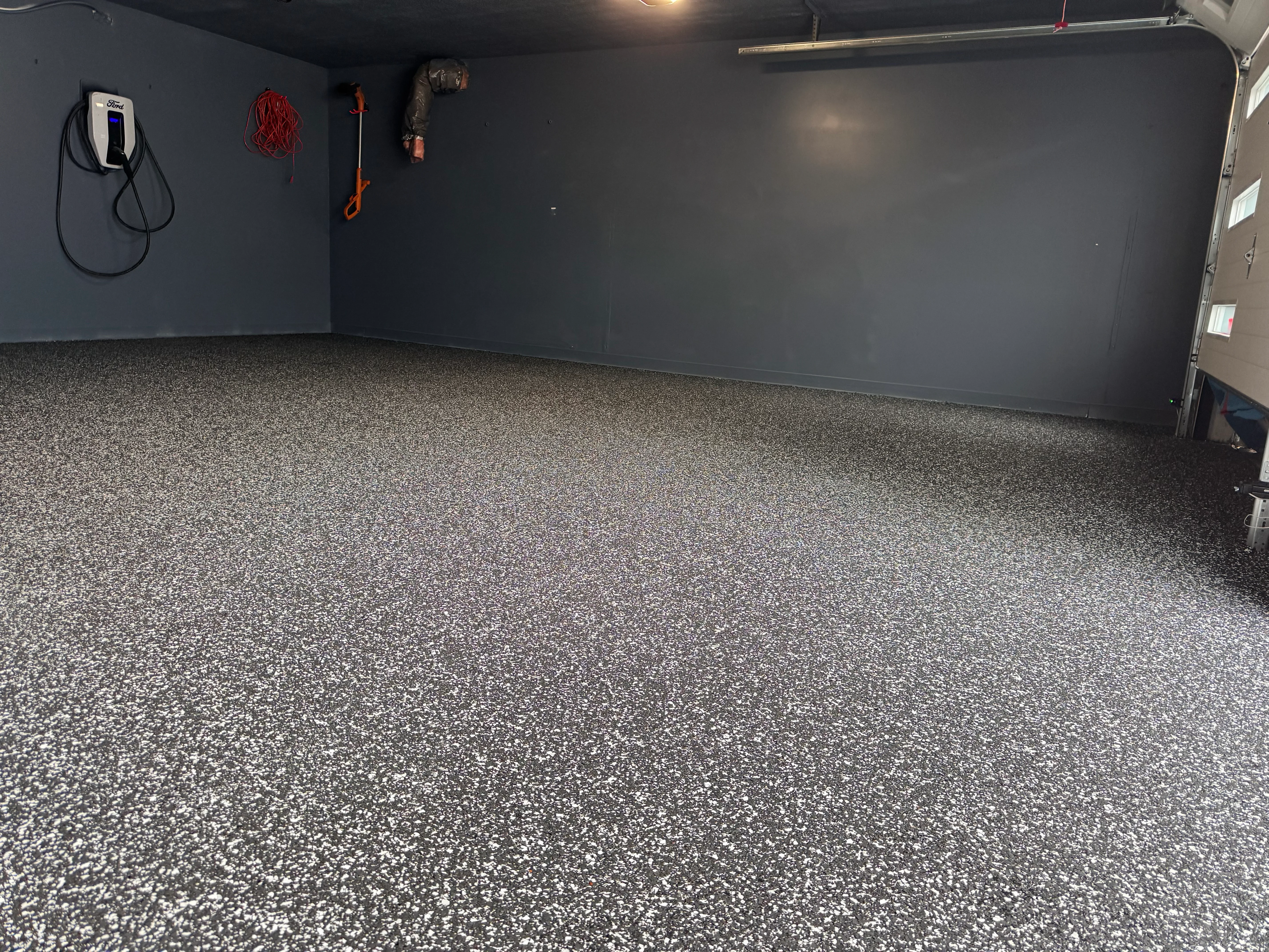 Gray speckled epoxy garage floor with dark walls and EV charger installation