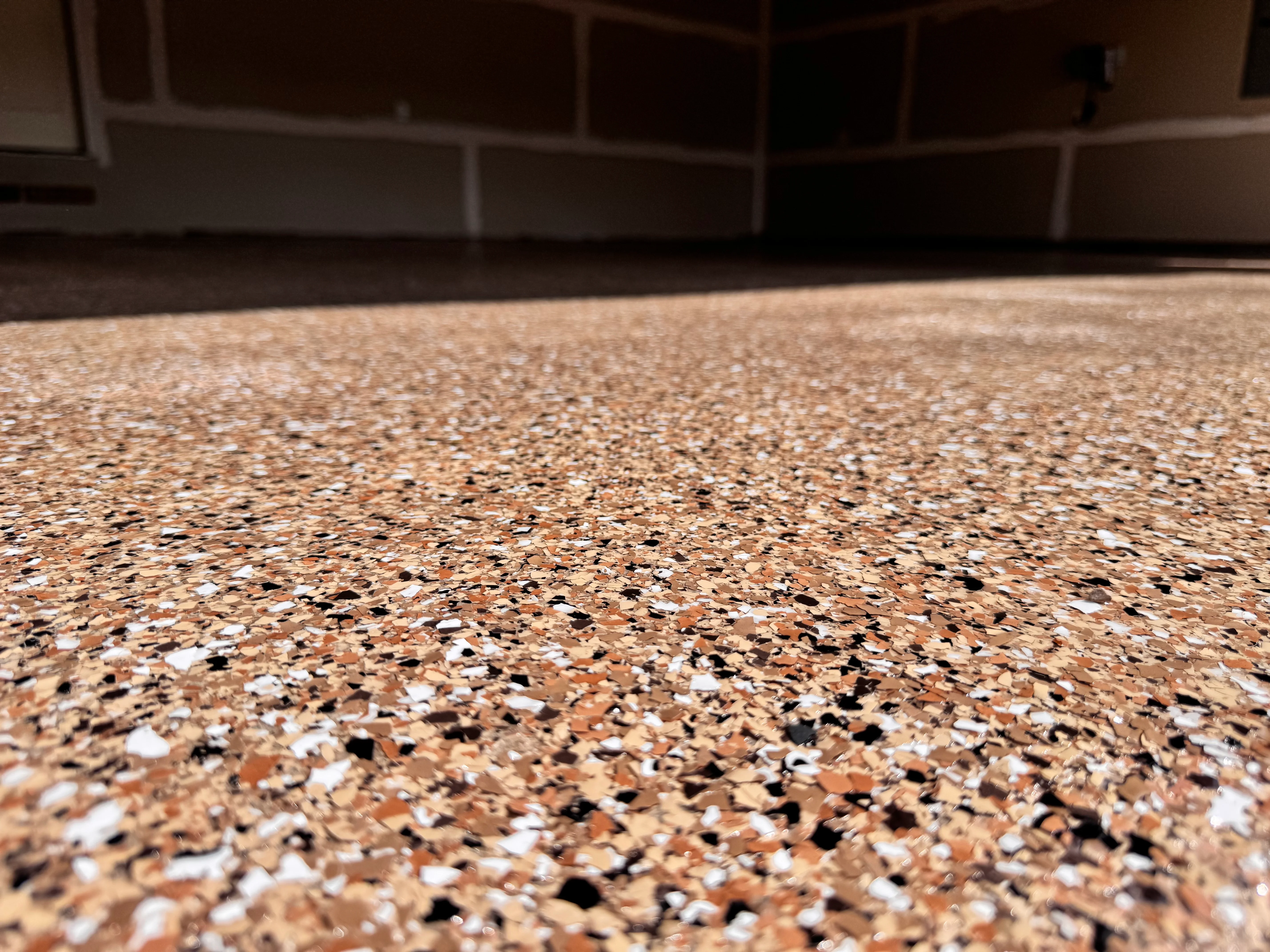 Close-up of speckled epoxy floor with tan, black, and white aggregate in garage setting