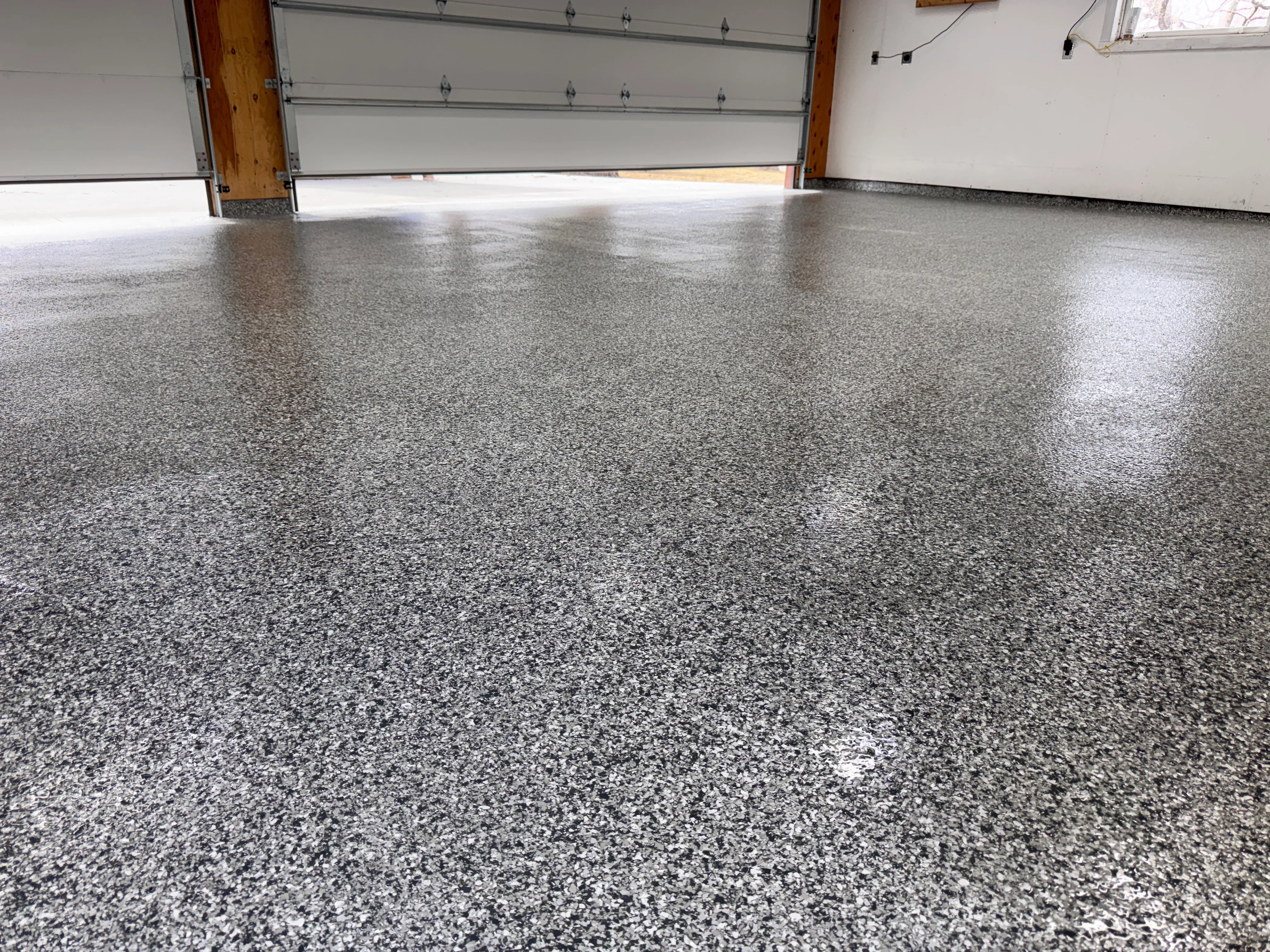 Polished gray speckled epoxy garage floor with glossy finish and white garage doors
