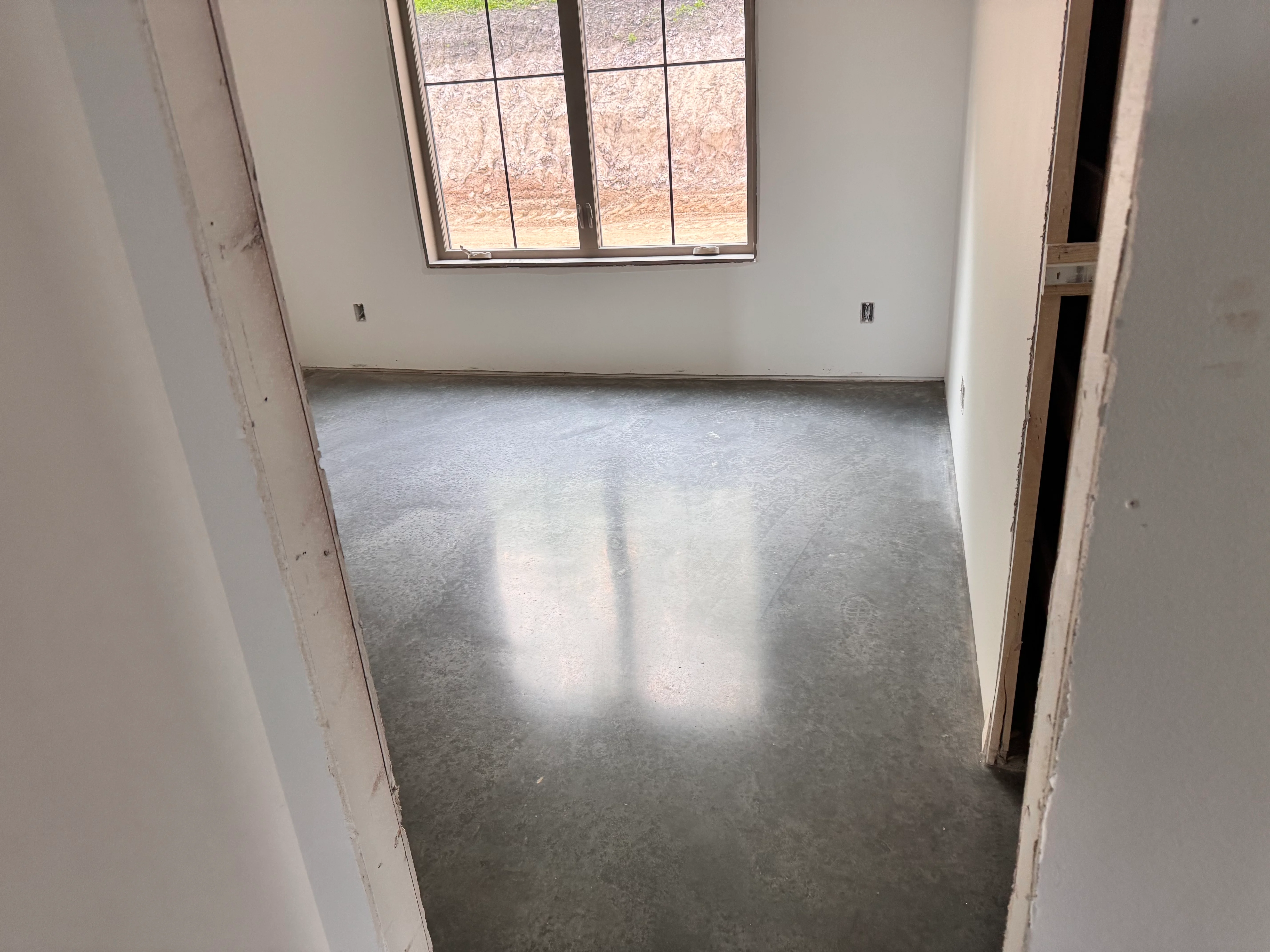 Polished concrete floor in bright room with large window and white drywall walls