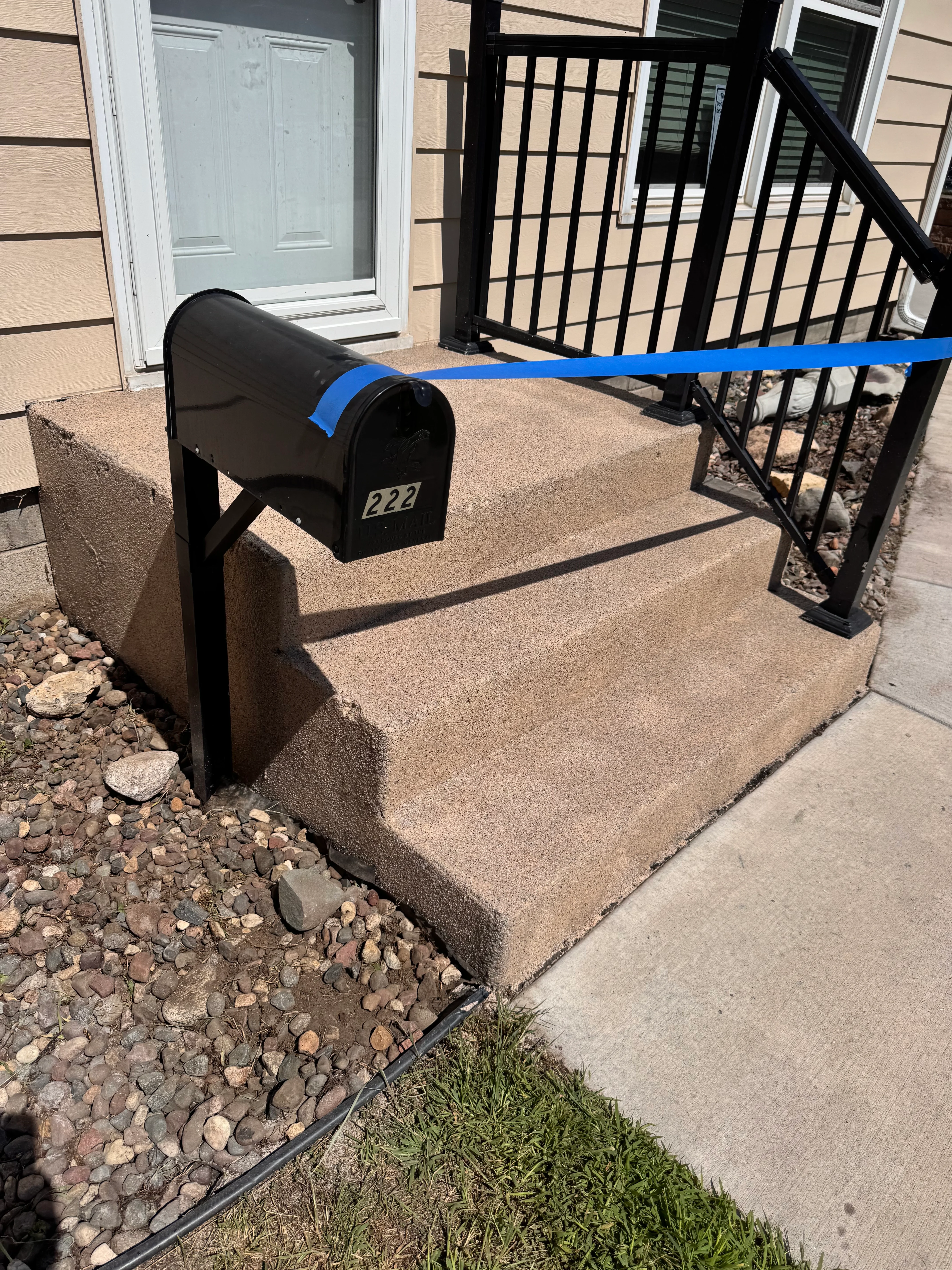 Black mailbox on epoxy-coated concrete entryway with metal railing and landscaping