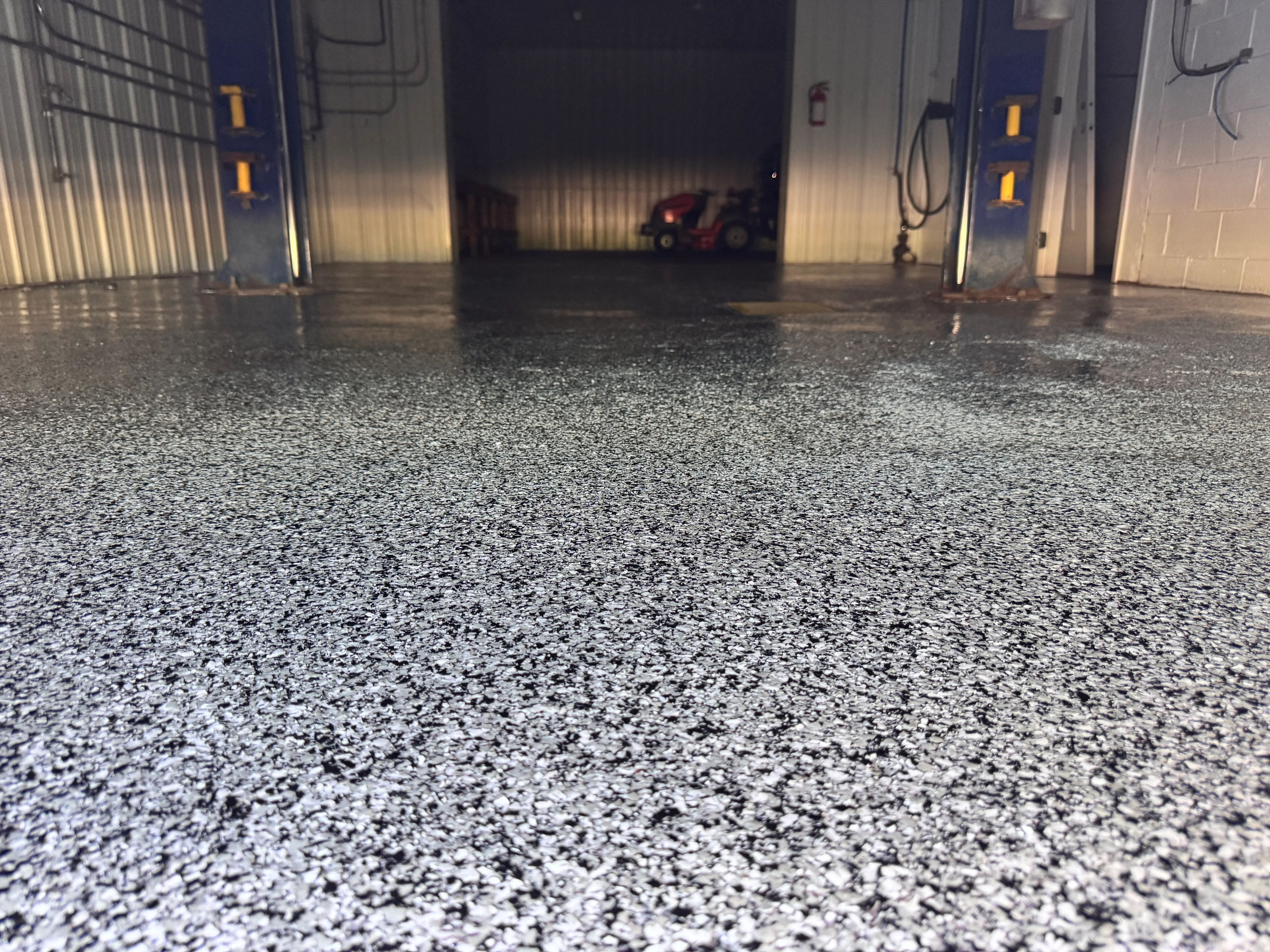 Polished gray speckled epoxy floor in commercial garage with blue overhead doors