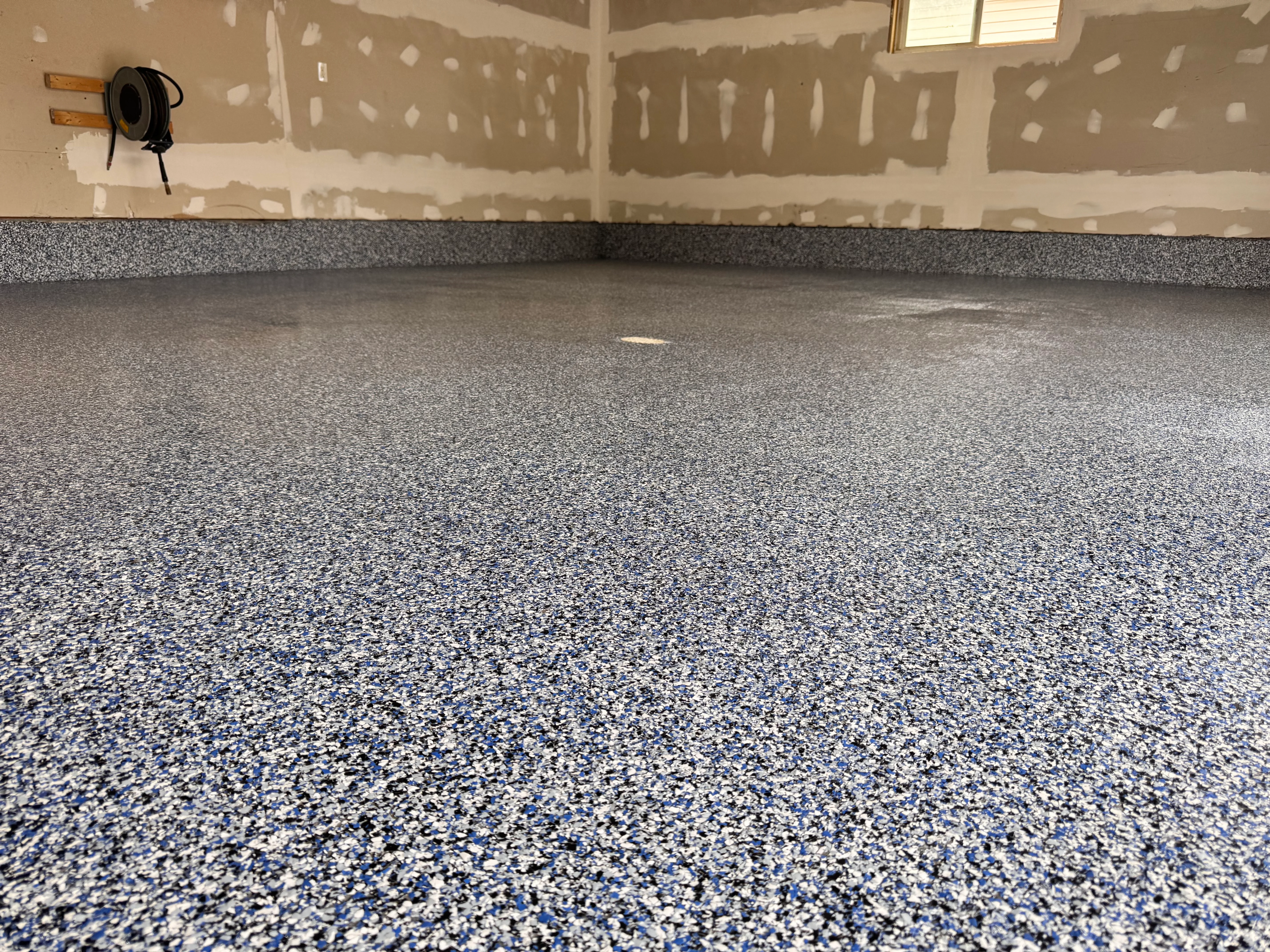 Finished garage epoxy floor with gray and blue aggregate finish and matching wall base coat