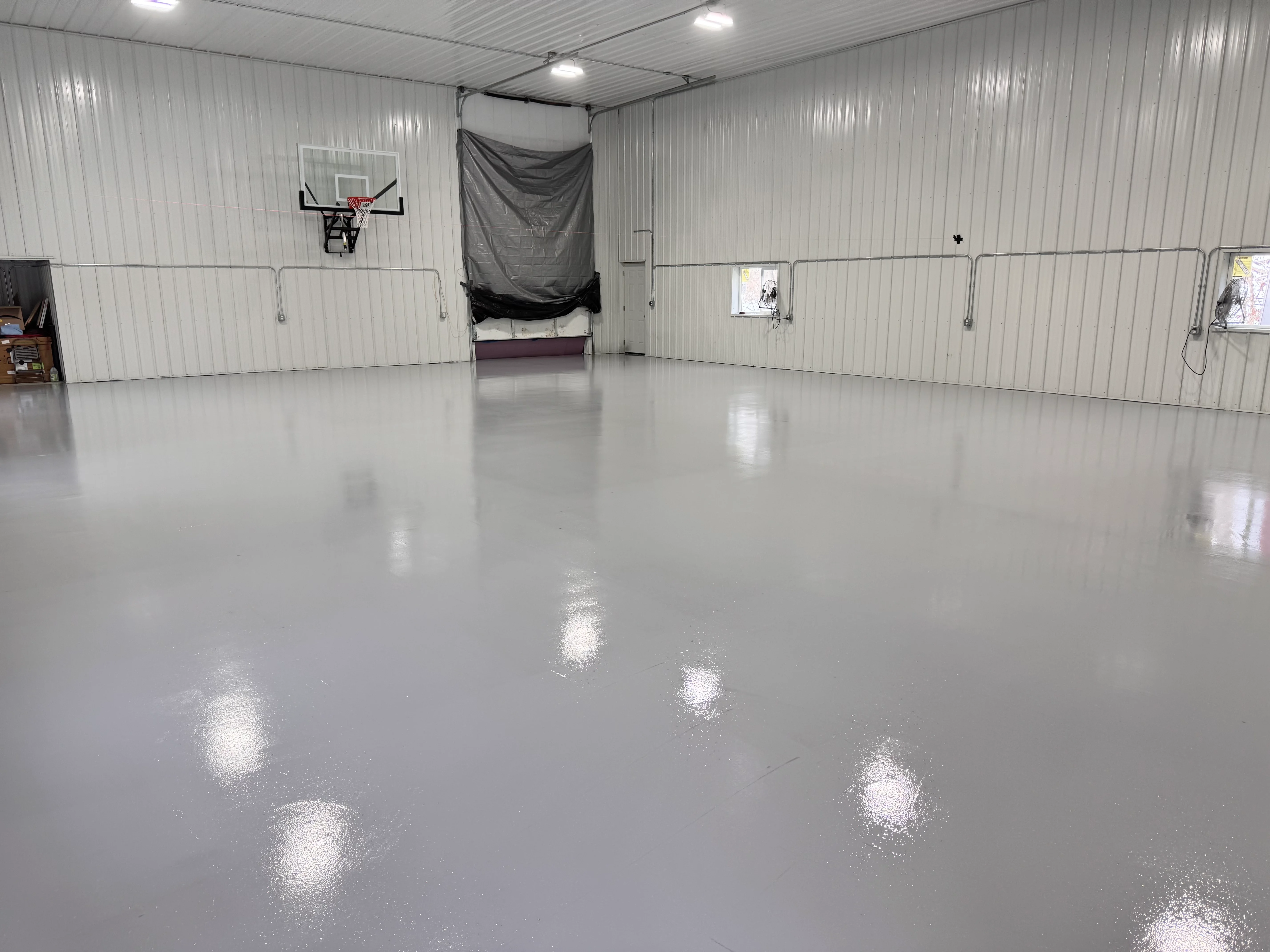 Metallic silver epoxy garage floor with reflective finish in metal building with basketball hoop