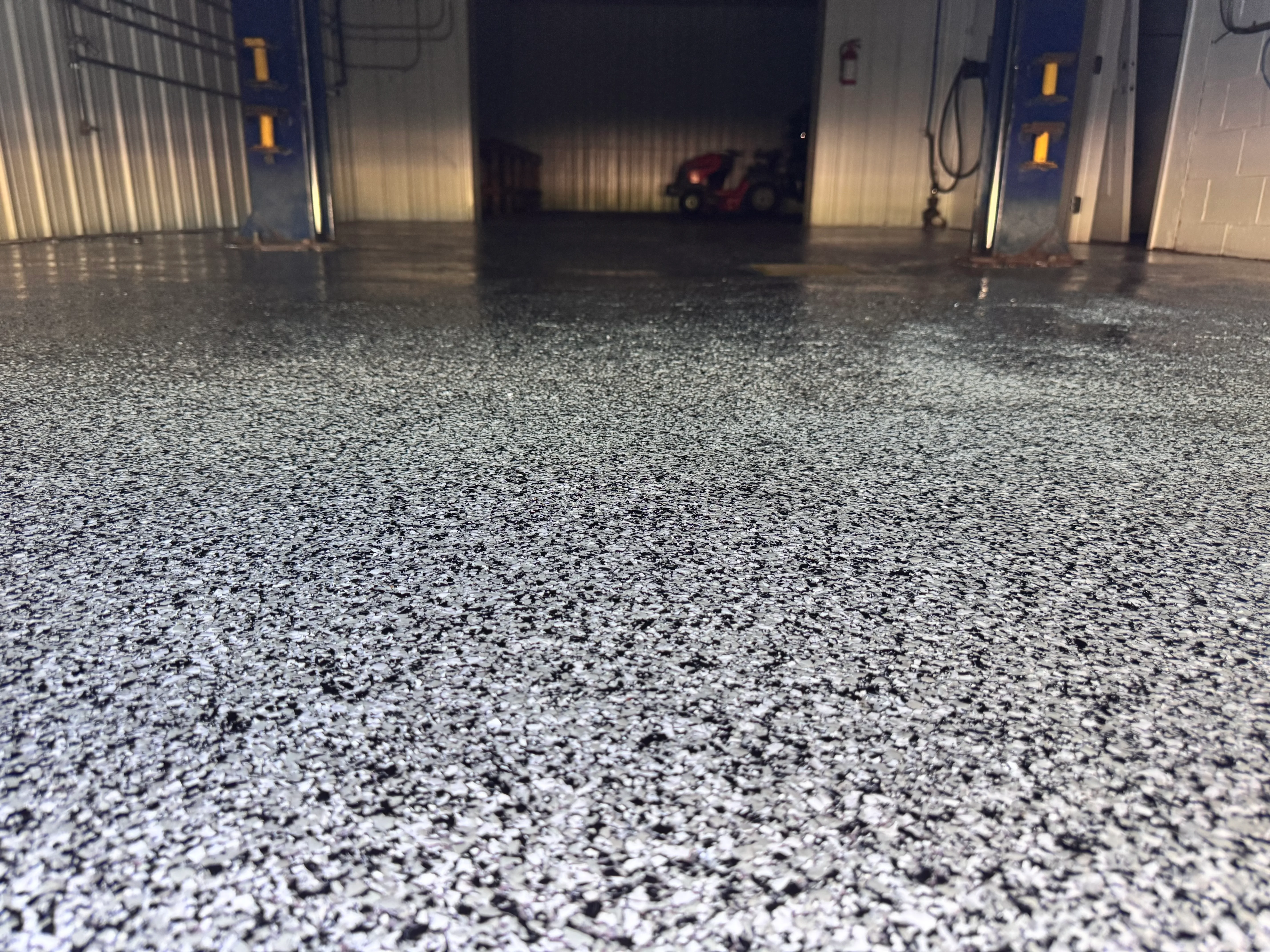 Speckled gray epoxy garage floor with overhead doors and industrial lighting